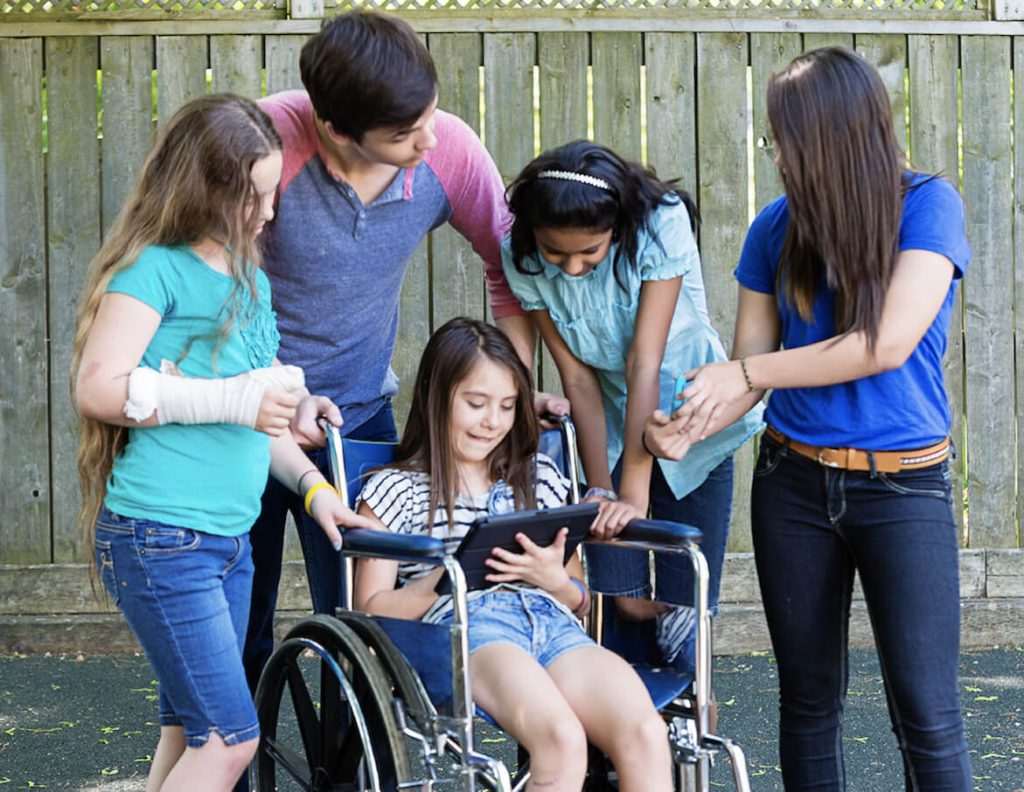 Kids looking at an ipad being held by a girl in a wheelchair