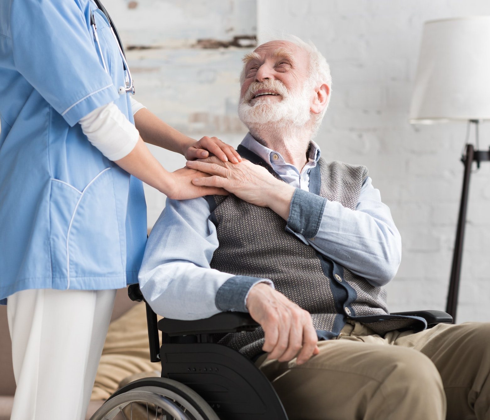 Happy and disabled senior man in wheelchair holding hands with doctor