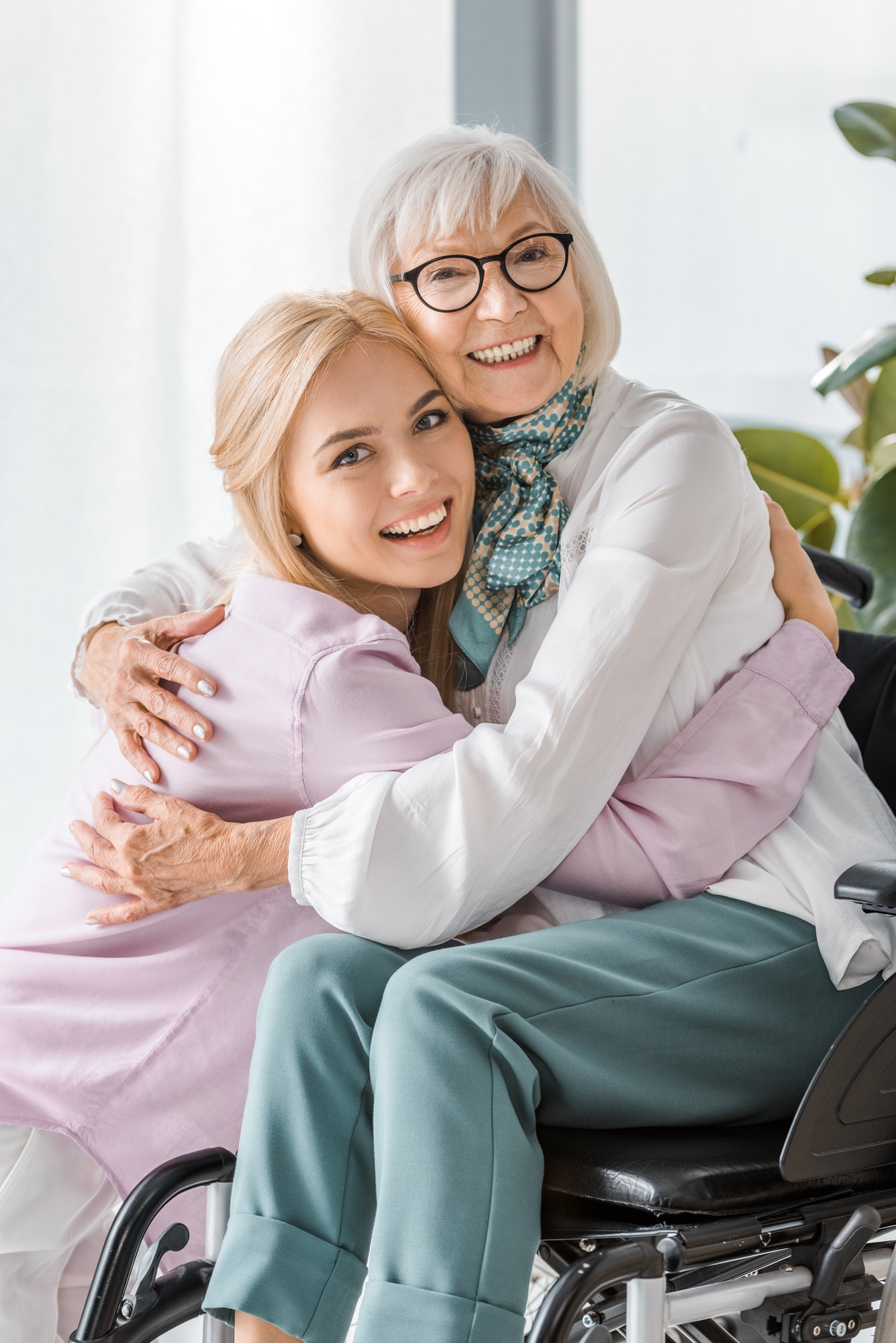 young cheerful woman hugging senior woman in wheelchair