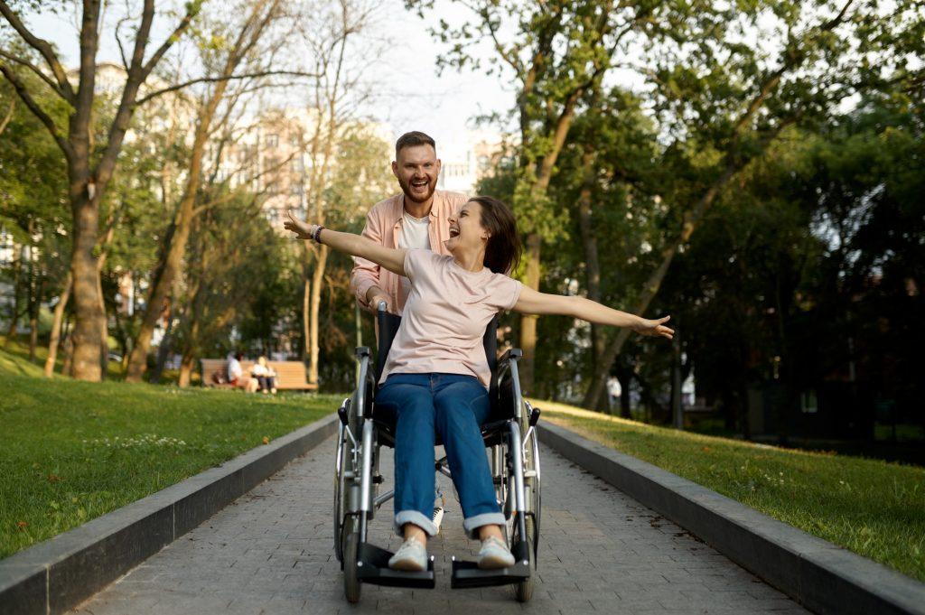 Cheerful love couple with wheelchair walks in park
