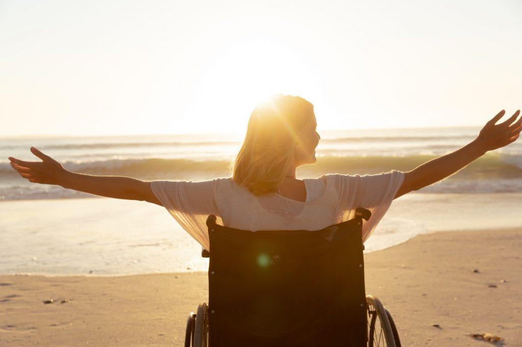 Rear view of woman on wheelchair with her arms wide open at the beach