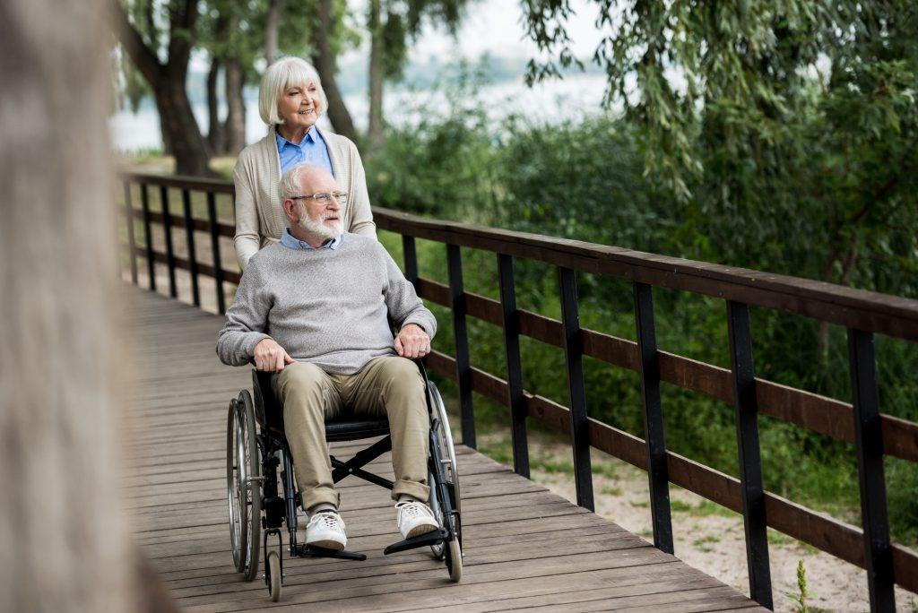 smiling senior woman with husband in wheelchair while walking in park