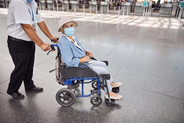 Lady in a protective mask sitting in a wheel chair being pushed by an employee