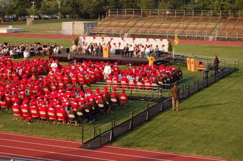Students in red sitting at a stage in a football field with a ramp in Fairlawn New Jersey for Graduation