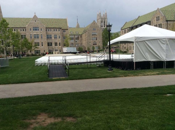 Outside on a green lawn, old school building in the background, white tent set up with chairs at Harvard for a graduation event