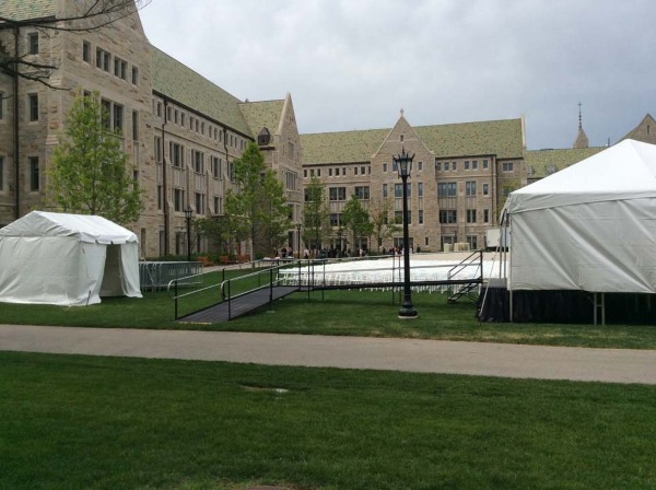 Old school buildings in background, on green lawn, white tent set ups, ramp leading into one of the large white tents for Harvard for a graduation event