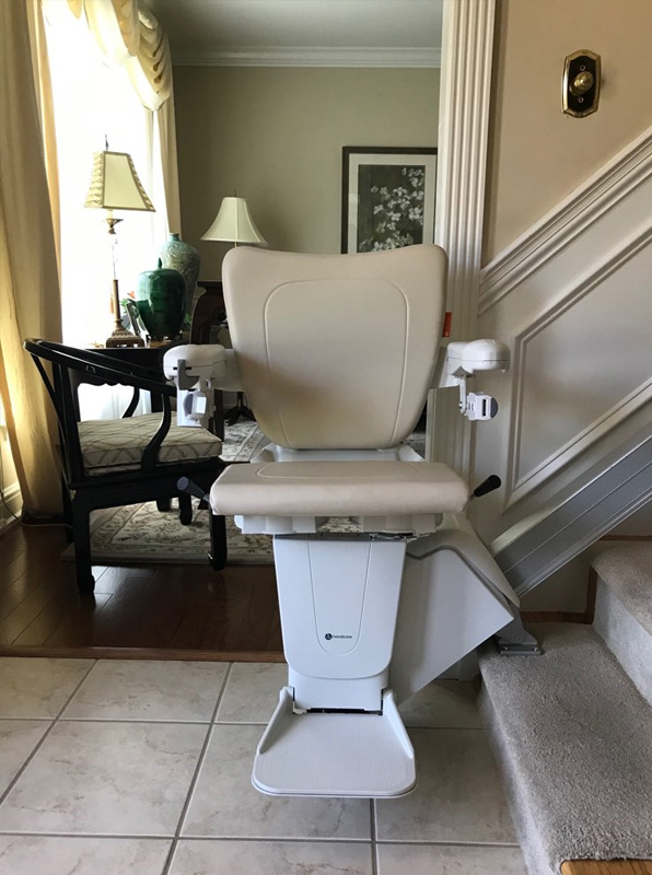 A straight stairlift is shown on a set of stairs. The lift is designed to carry individuals with limited mobility up and down stairs safely and comfortably. It features a sturdy seat, armrests, and footrest, as well as safety sensors and a durable weather-resistant construction to withstand outdoor elements.