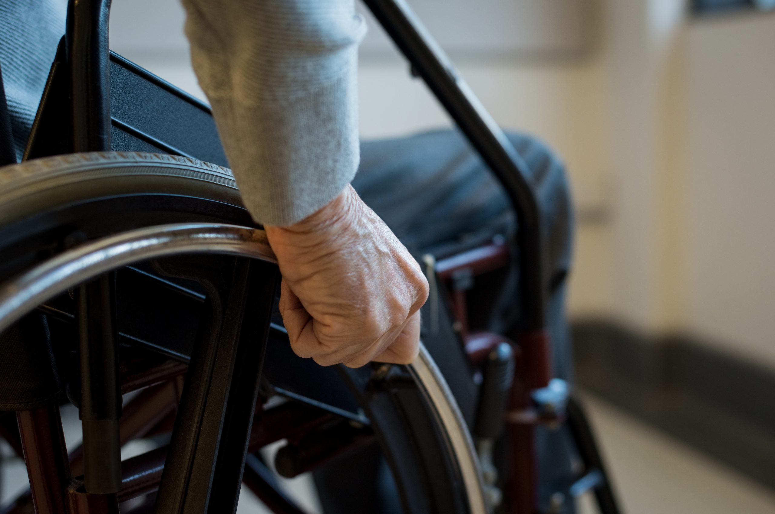 A close-up of an older man's hand on the wheel of his wheelchair, pushing forward.