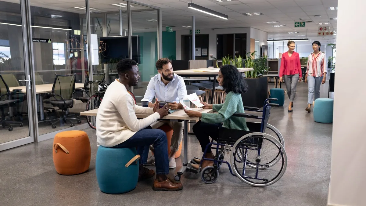 a group of people working in an office. one person is in a wheelchair, another is sitting on a stool.