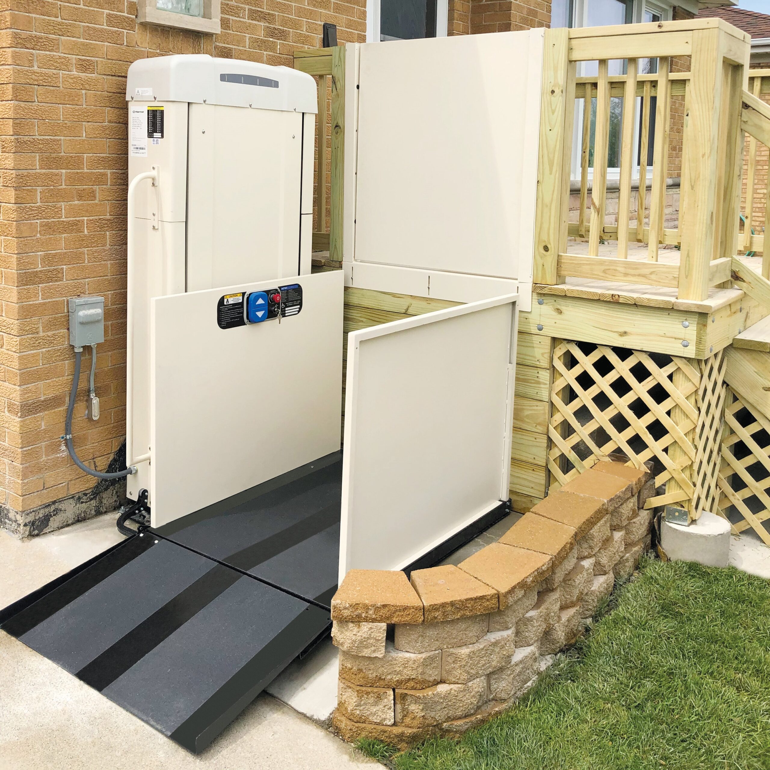 A Harmar Highlander II vertical platform lift installed outdoors, providing safe wheelchair access to an elevated porch with sturdy side rails and a smooth lift platform.