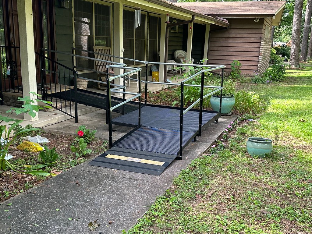 a metal amramp ramp in front of a one story brown house leading up to the front door, with a grass yard to the right