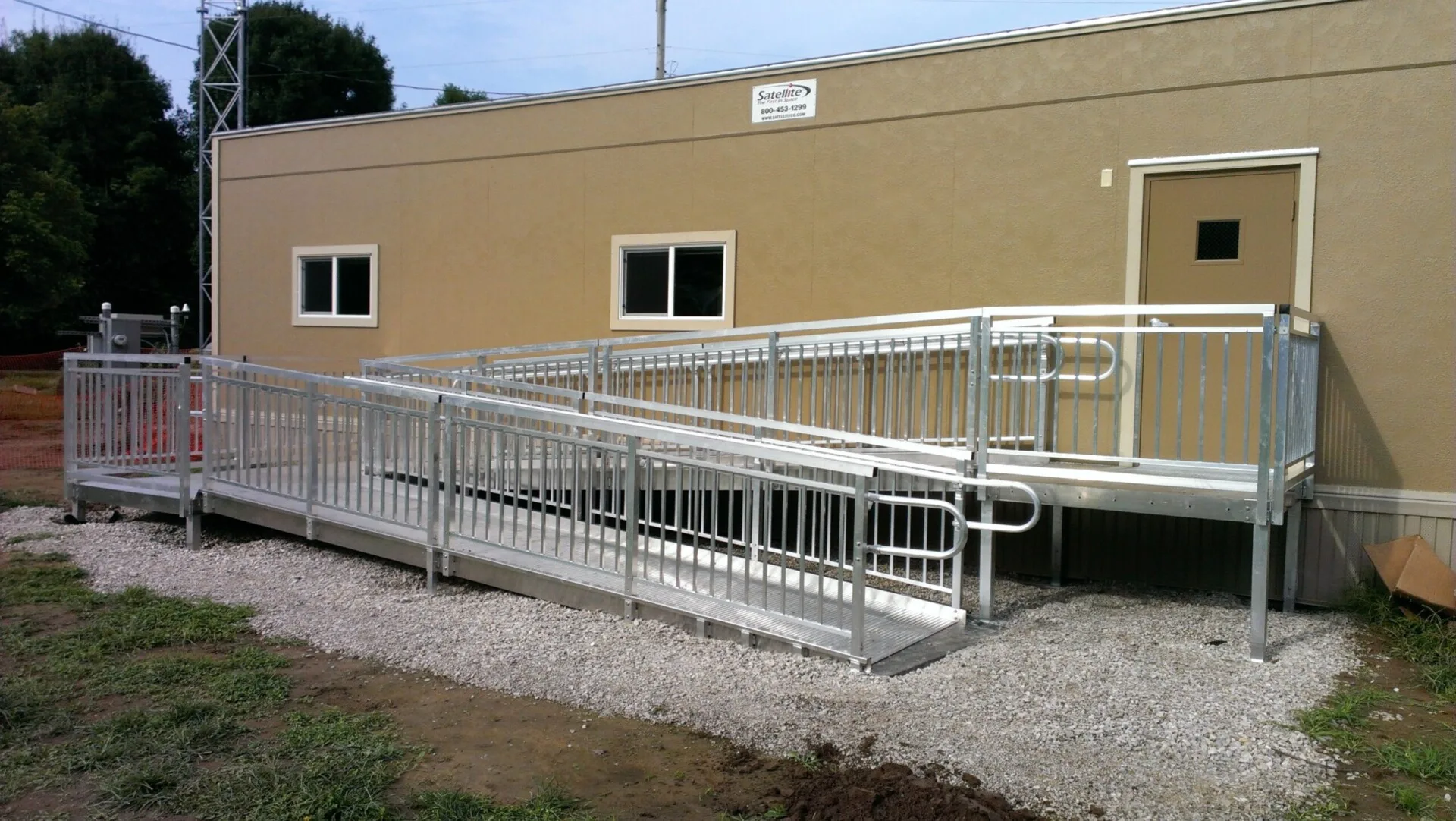 a brown building with a commercial metal ramp leading from a walkway to the building entrance