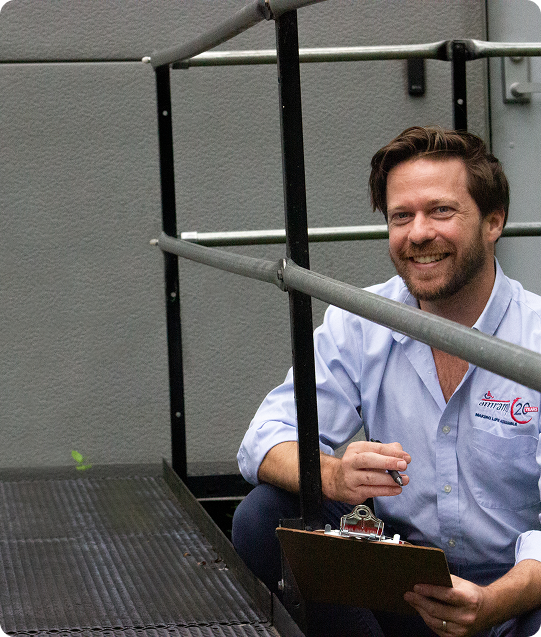 a man in a blue shirt and a beard, smiling as he kneels down to perform a routine maintenance check on a ramp