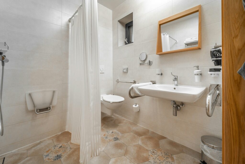 Accessible bathroom with a wall-mounted shower seat, grab bars, roll-under sink and open floor space.