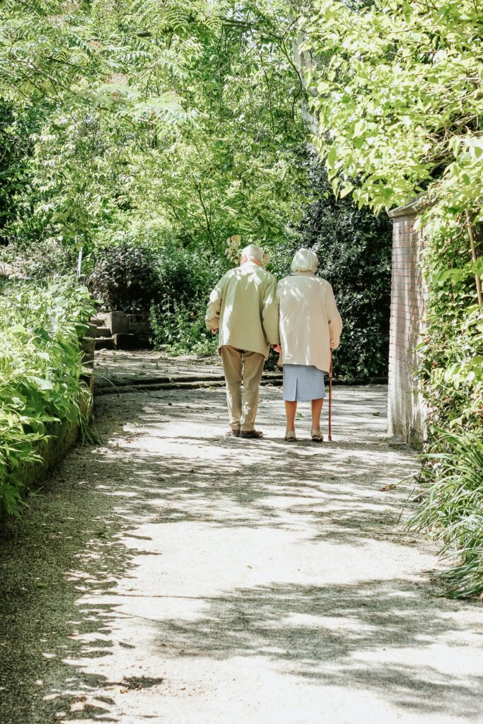 Older couple walking together along a tree-lined path while maintaining an active and independent lifestyle.