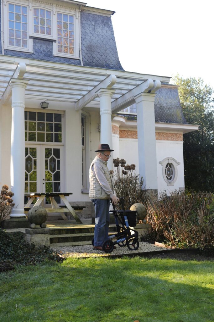 Older adult using a walker outside their home while maintaining independence and mobility.