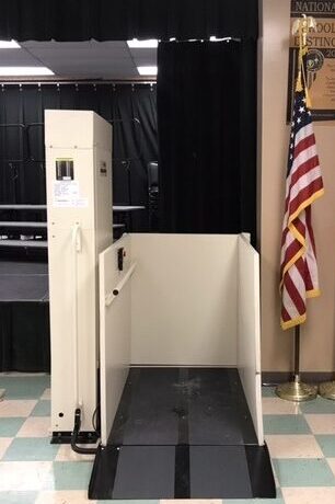 Commercial vertical platform lift installed beside an indoor stage to provide accessible wheelchair access.