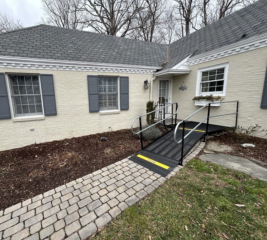 Amramp modular wheelchair ramp installed at the front entrance of a brick home with a paved walkway for accessible entry.