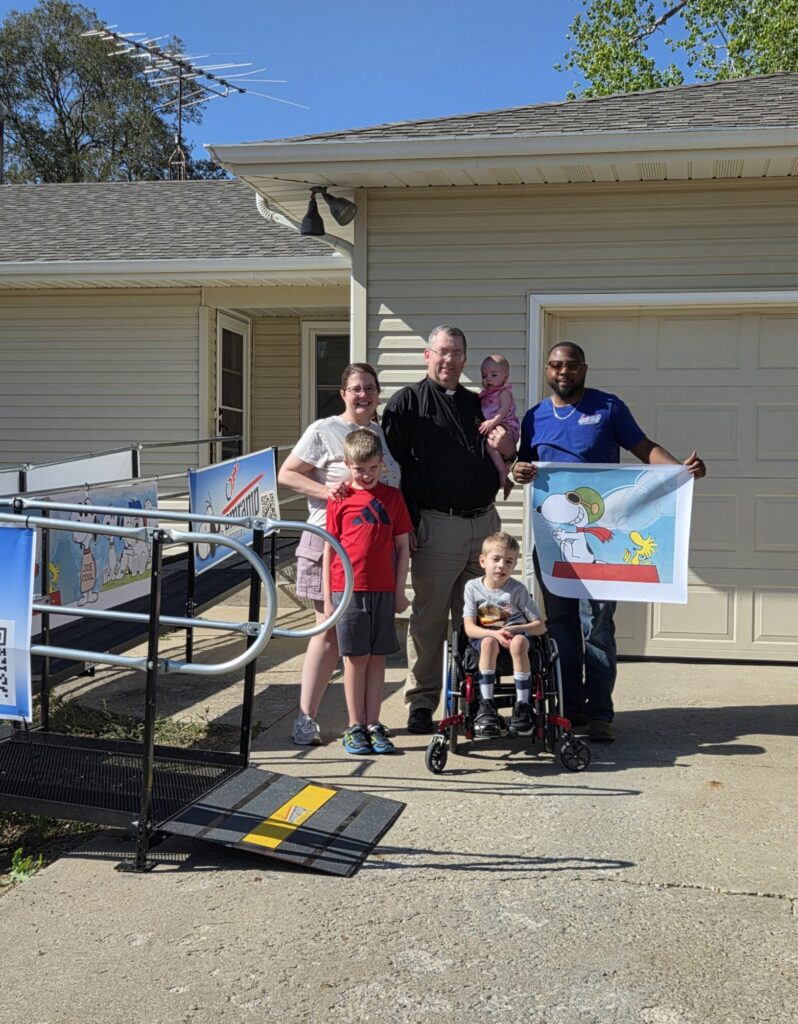 Amramp Kansas City owner stands with a family beside a newly installed wheelchair ramp outside their home.