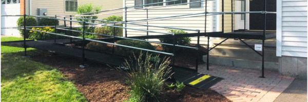 A steel switchback style wheelchair ramp in front of a house with lush vegetation