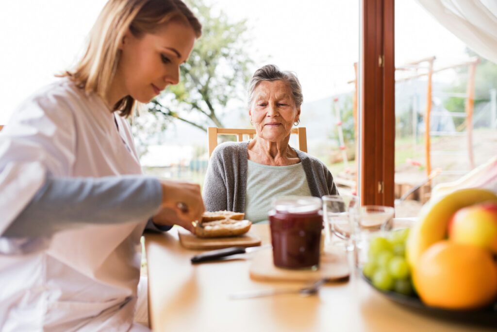 Caregiver assisting an older adult with meal preparation and dining support in a residential care setting.