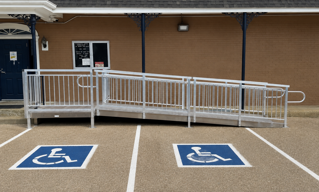 Commercial aluminum wheelchair ramp installed outside a building entrance with accessible parking spaces.