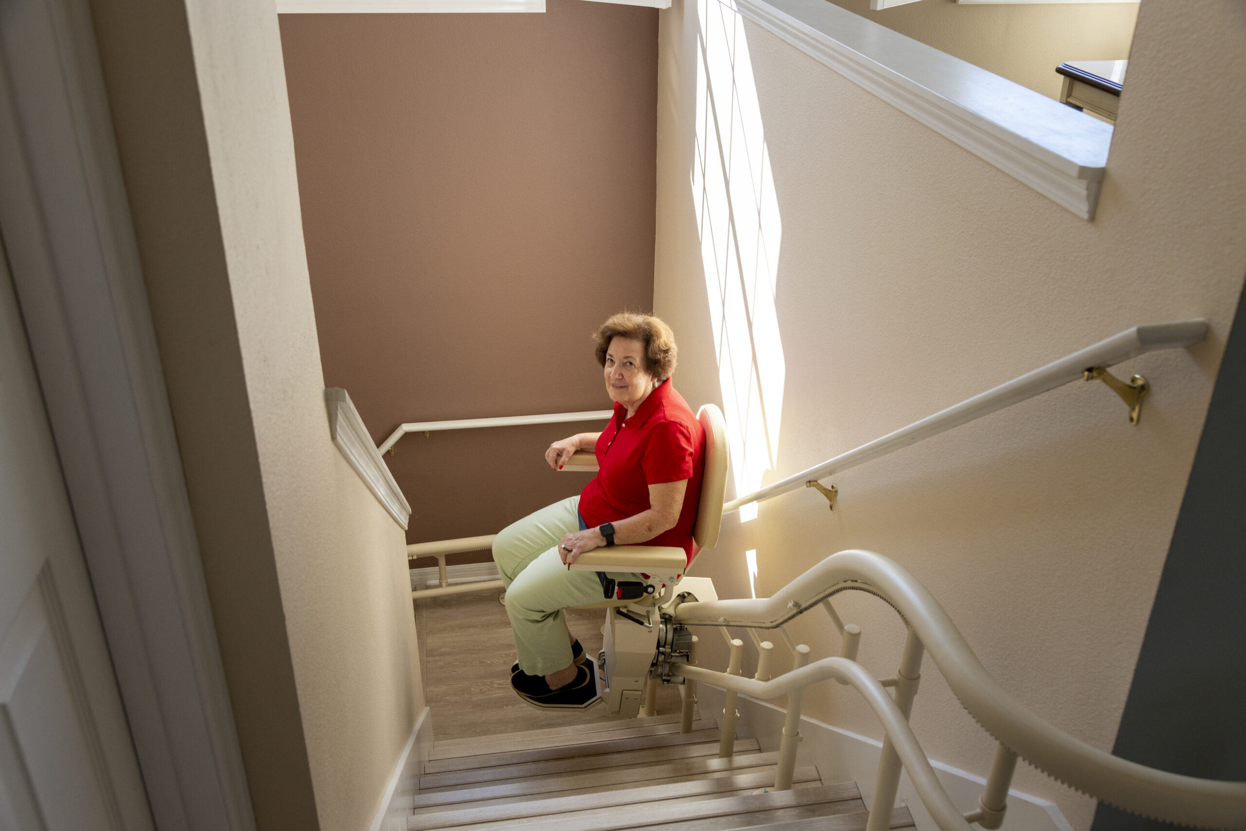 Older woman riding a curved stair lift along a staircase in her home, providing safe and comfortable access between floors.