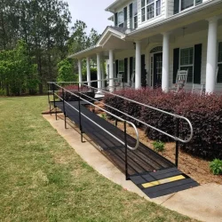 Long modular wheelchair ramp installed alongside the front porch of a two-story home with white columns.