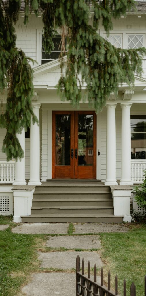Front entrance of a white house with several steps leading to wooden double doors.