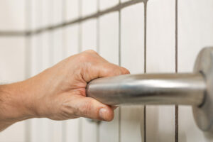A hand holding a brushed nickel grab bar with white subway style tile in the background
