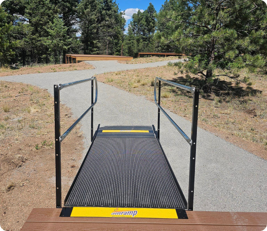 a photo of a ramp in an outdoor setting with pine trees and a cement walking path