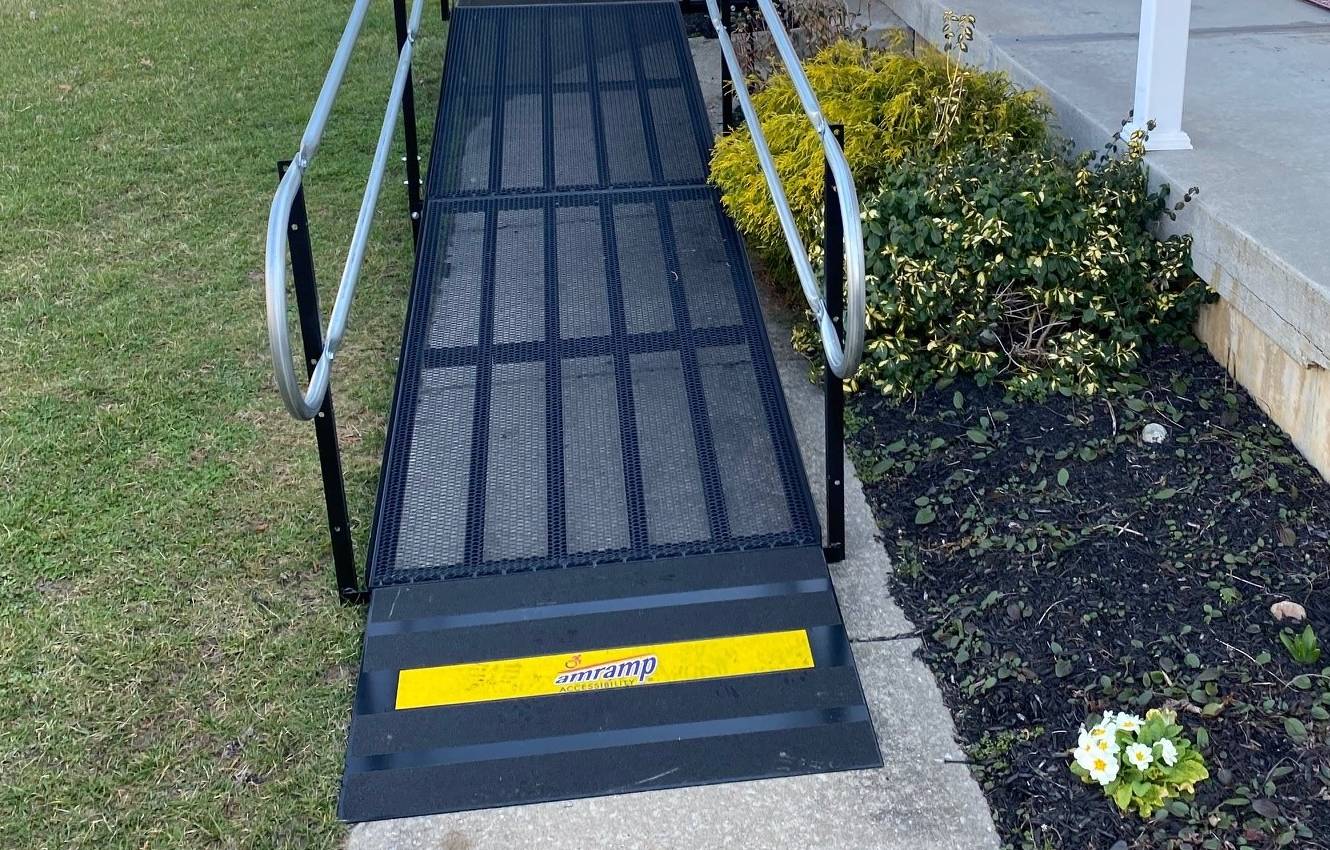 a black steel modular ramp leading from a sidewalk up to a house porch.