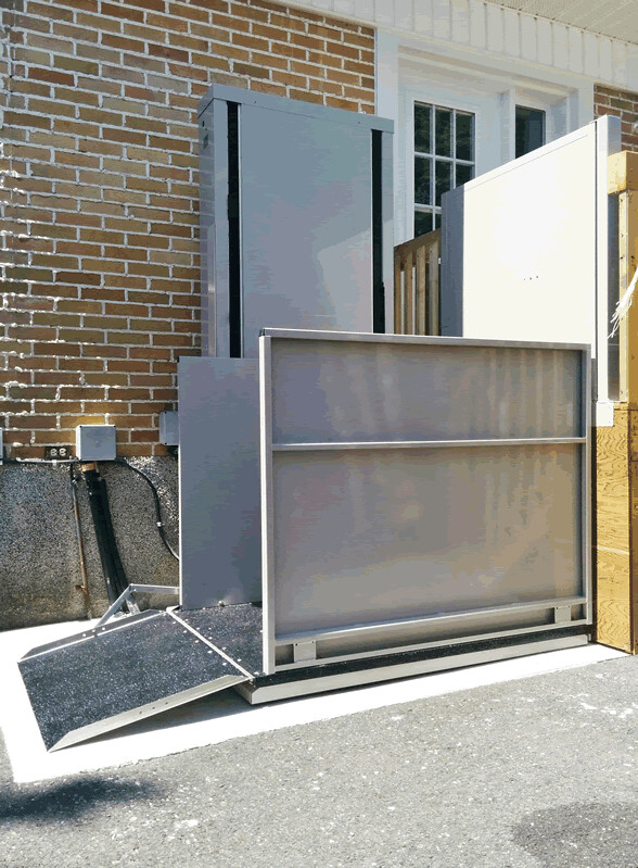 Outdoor vertical platform lift installed at a building entrance to provide wheelchair-accessible entry.