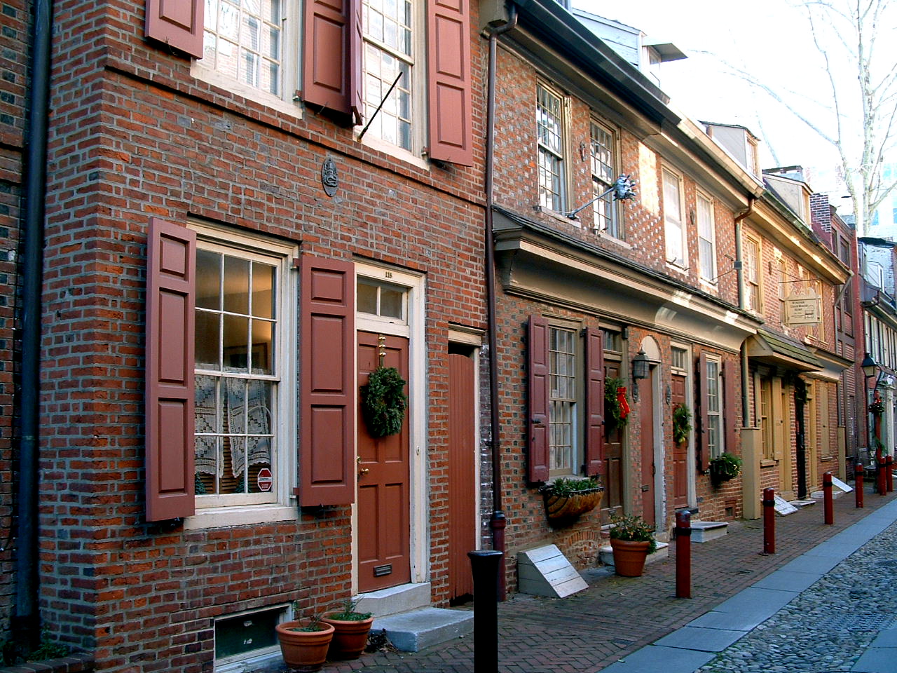 Historic Philadelphia brick row homes with narrow front entrances, raised doorsteps, and traditional shutters along a cobblestone street.