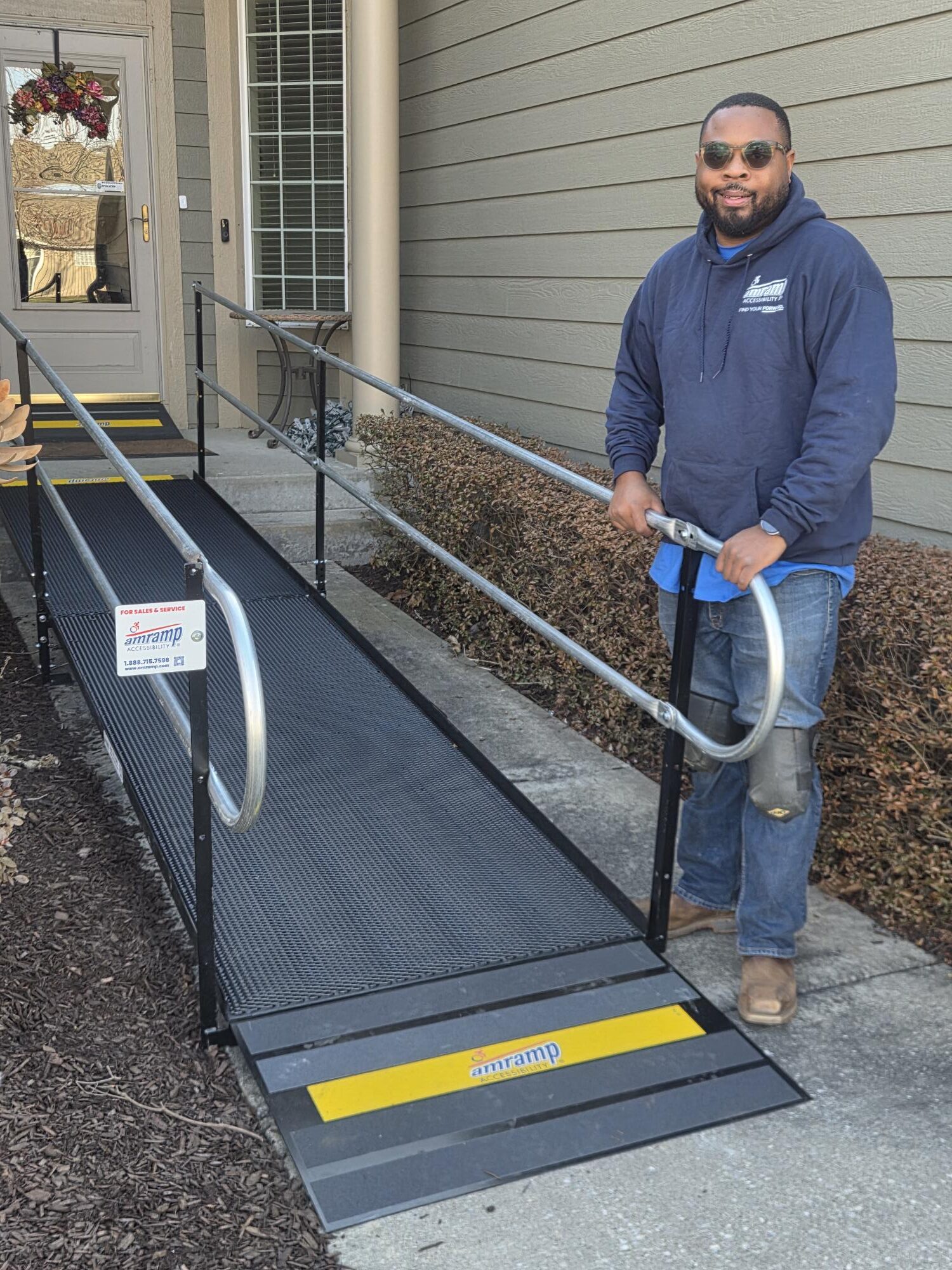 Owner of Amramp Accessibility of Kansas City, Quintin Clark, stands next to installed steel wheelchair accessibility ramp providing access to family at their home