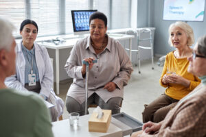 A group of women sitting in a circle in a clinical type of setting listening to someone speak