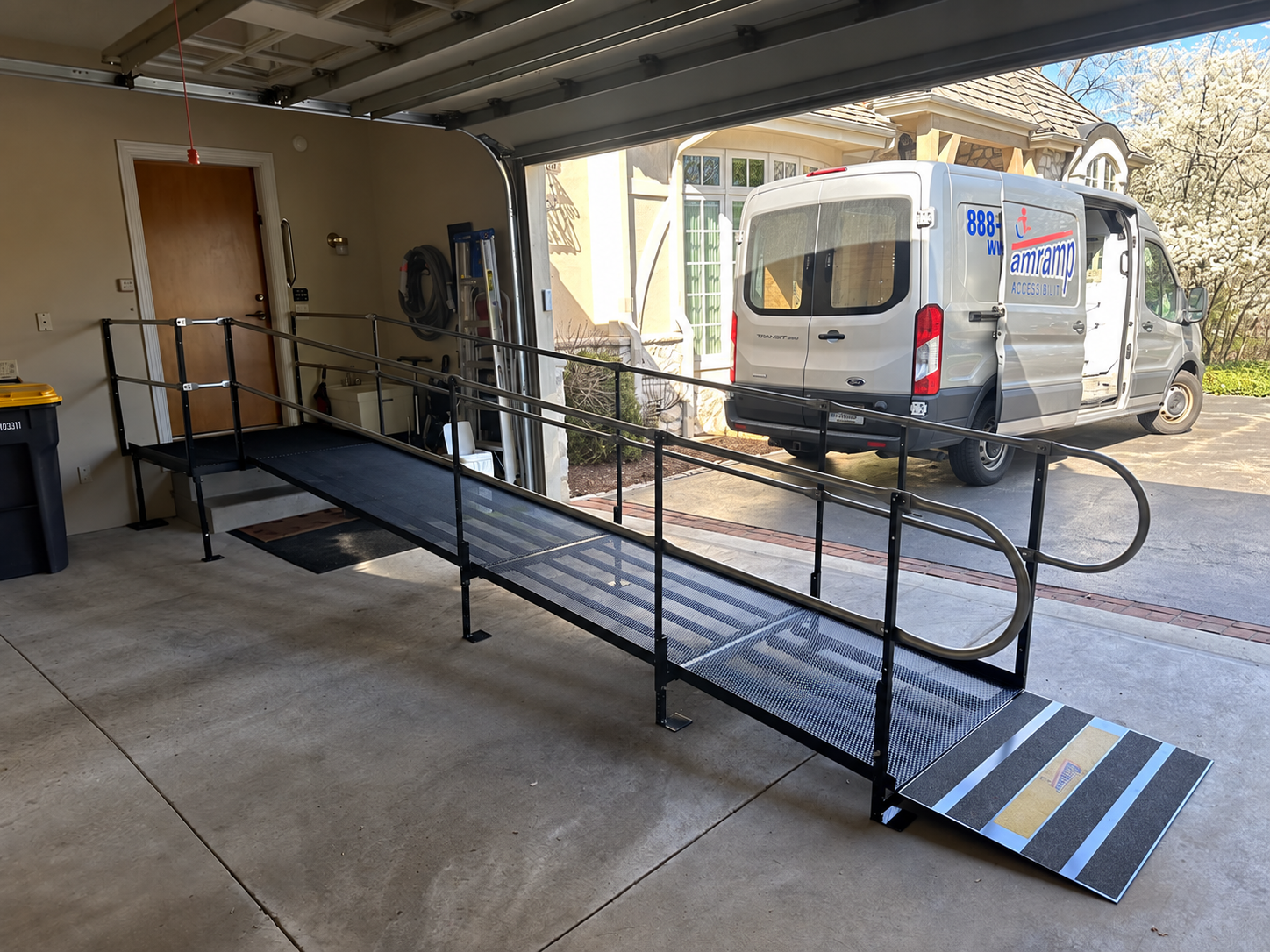 Black modular wheelchair ramp installed inside a residential garage with an Amramp service van parked outside